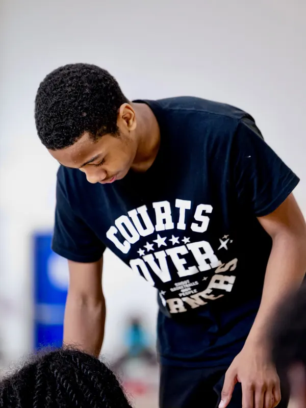 A young coach in a black Courts Over Corners SBNP tee